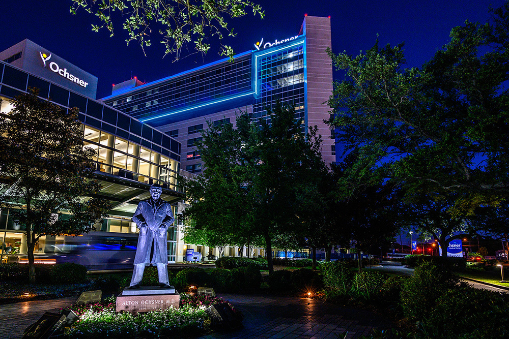 Ochsner Statue at night with blue lighting the building behind