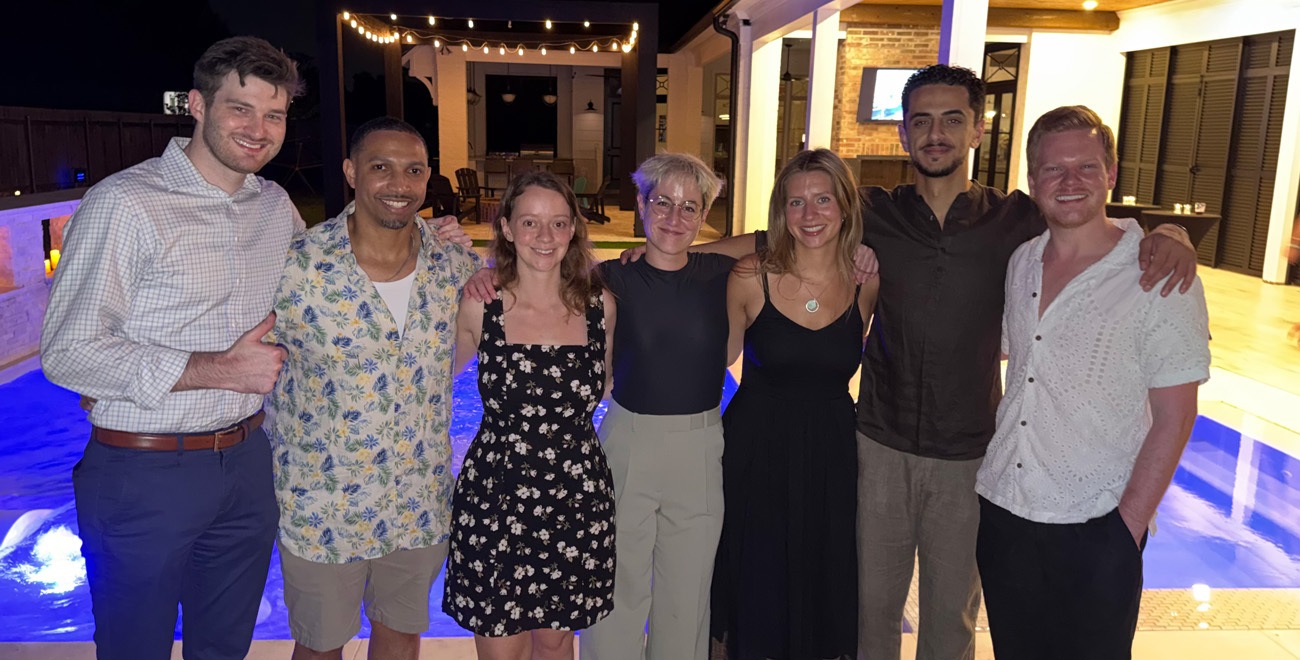 Group of Ochsner general surgery housestaff and residents posing together by a lit swimming pool at night.
