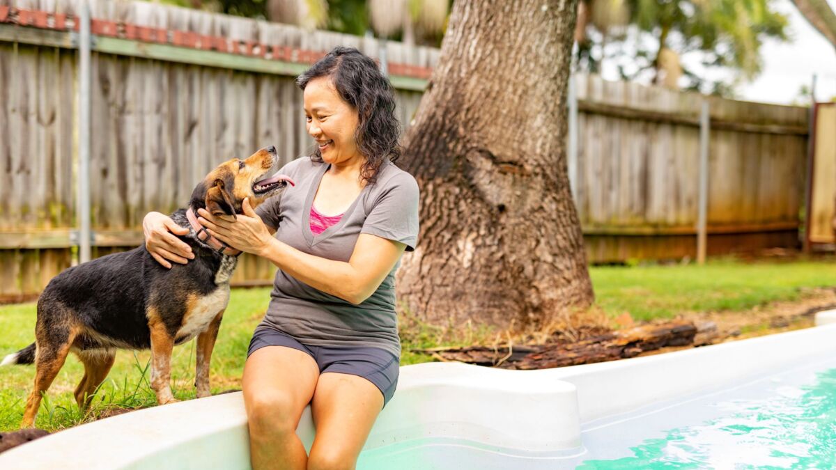 Lady with legs in pool smiling at dog