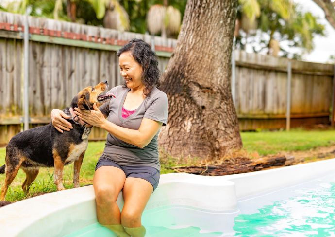 Lady with legs in pool smiling at dog