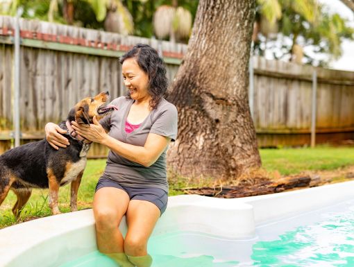 Lady with legs in pool smiling at dog