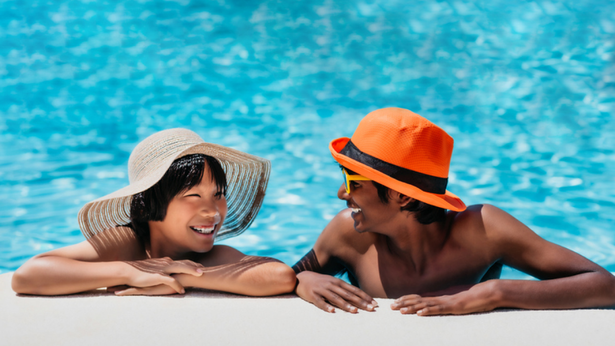 Two boys in the pool with hats on looking at each other and smiling