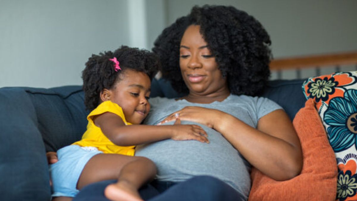 Pregnant mom lying on the couch with her daughter touching her belly.