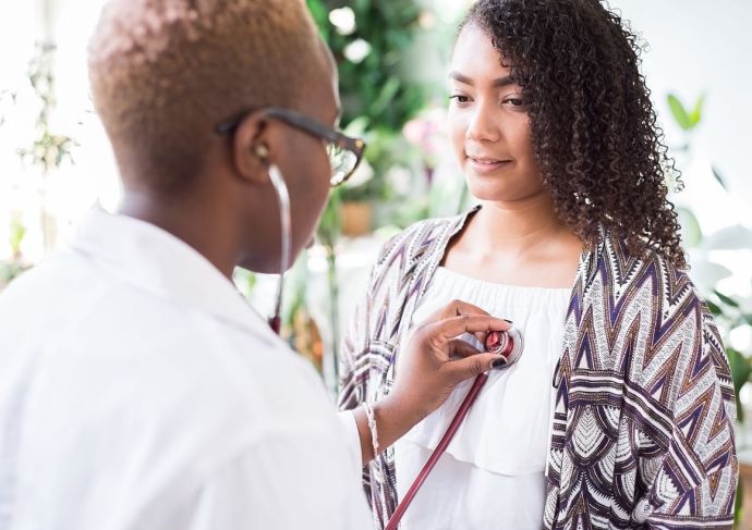 Black female doctor using a stethoscope to conduct exam for a patient