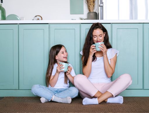 Mother and daughter sitting on the ground in the kitchen drinking coffee together
