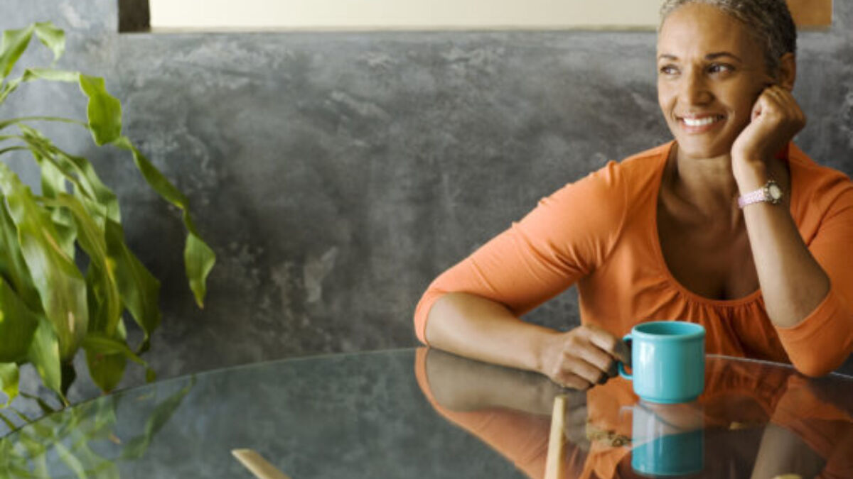 Woman sitting at a table smiling, with a beverage in her hand