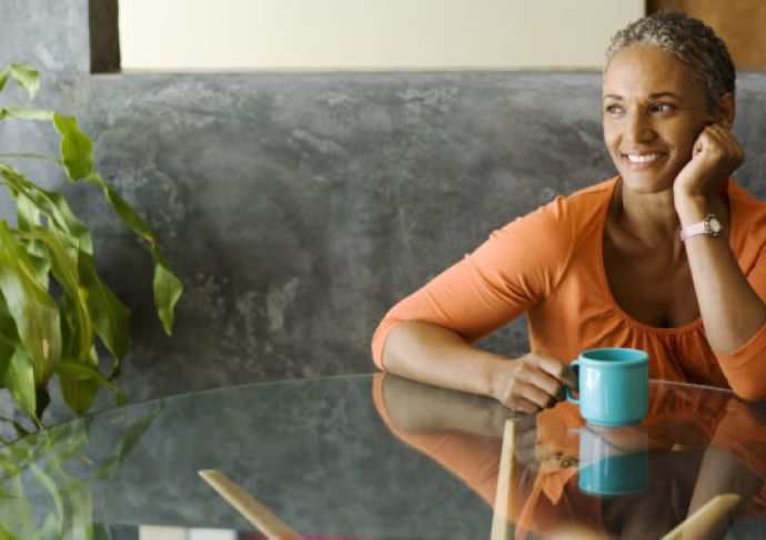 Woman sitting at a table smiling, with a beverage in her hand