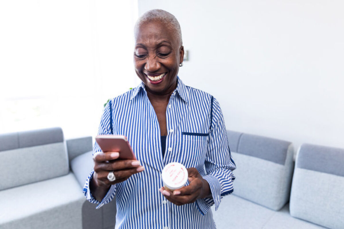 Smiling woman with a phone and pills in her hands