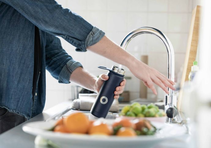 Woman filling water bottle from faucet in kitchen