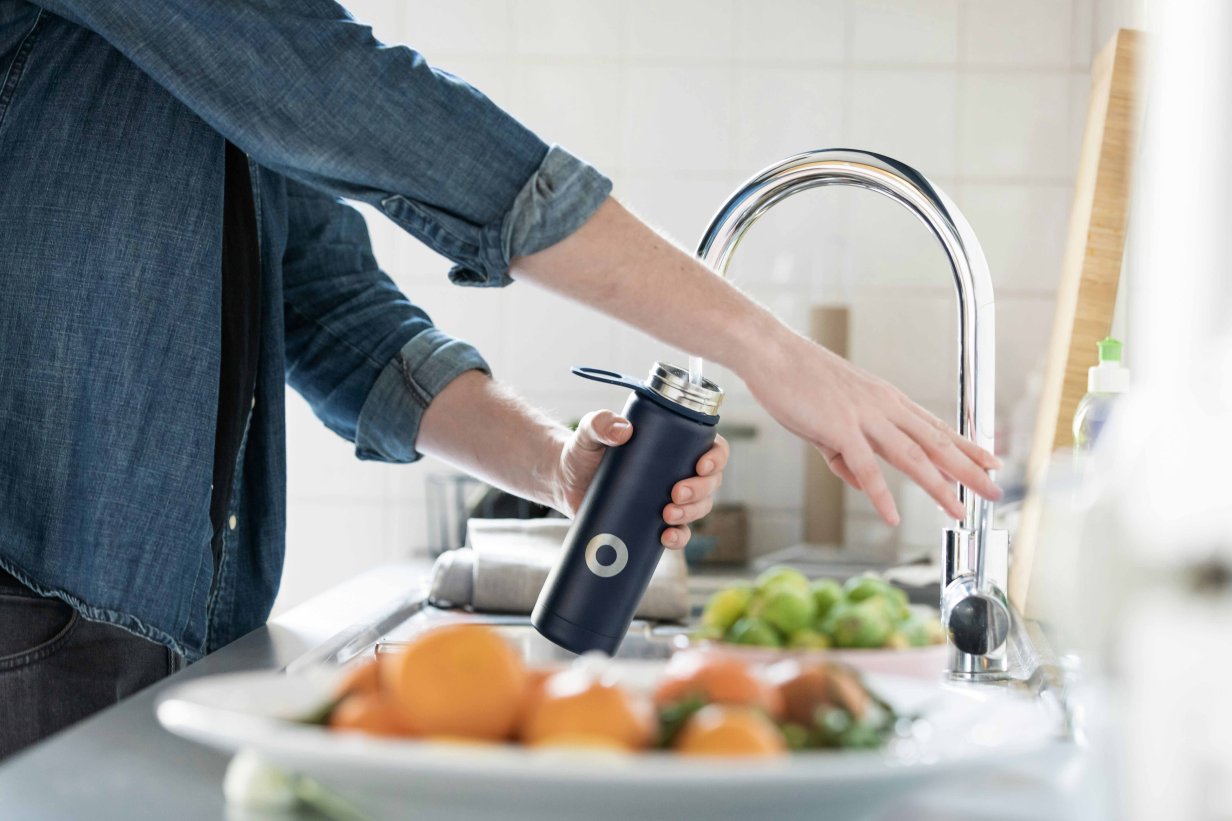 Woman filling water bottle from faucet in kitchen