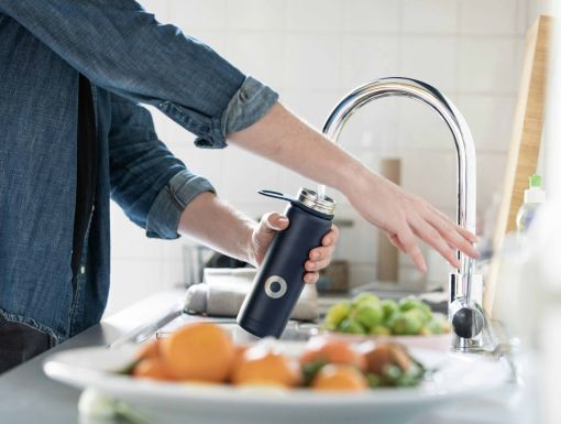 Woman filling water bottle from faucet in kitchen