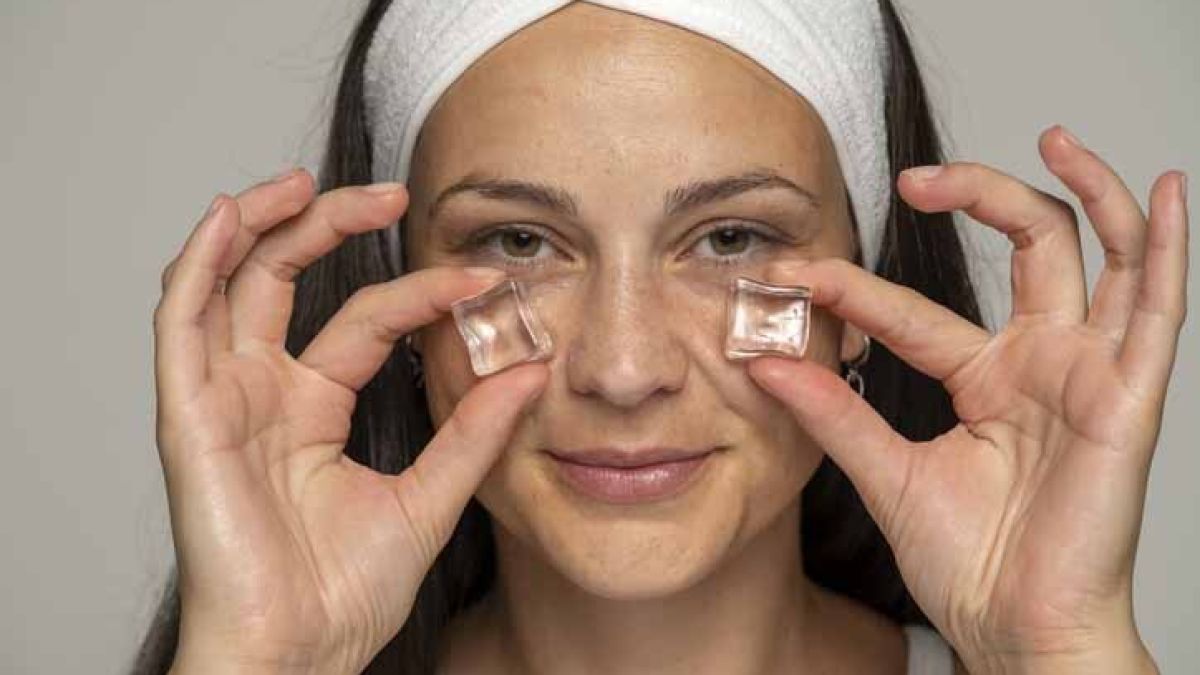 Young woman pressing ice cubes under eyes