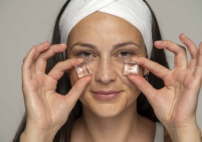 Young woman pressing ice cubes under eyes