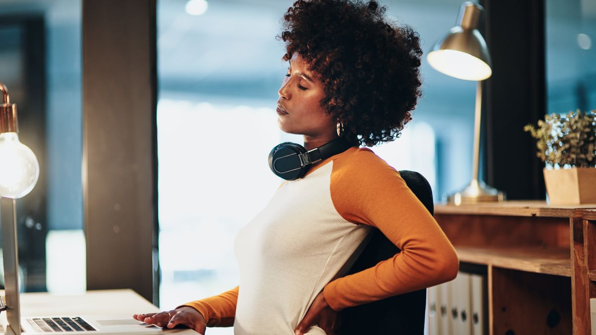 Woman at desk holding lower back