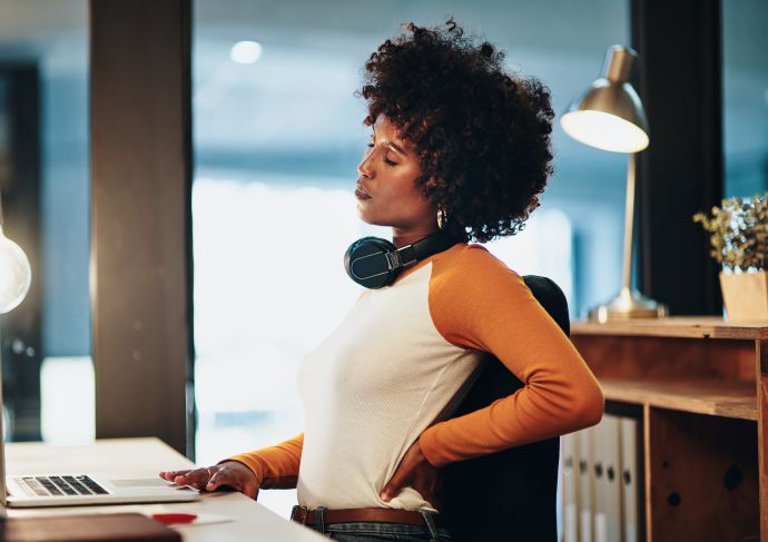 Woman at desk holding lower back