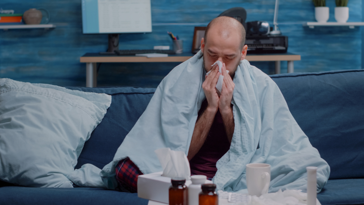 Man sitting on the couch at night blowing his nose