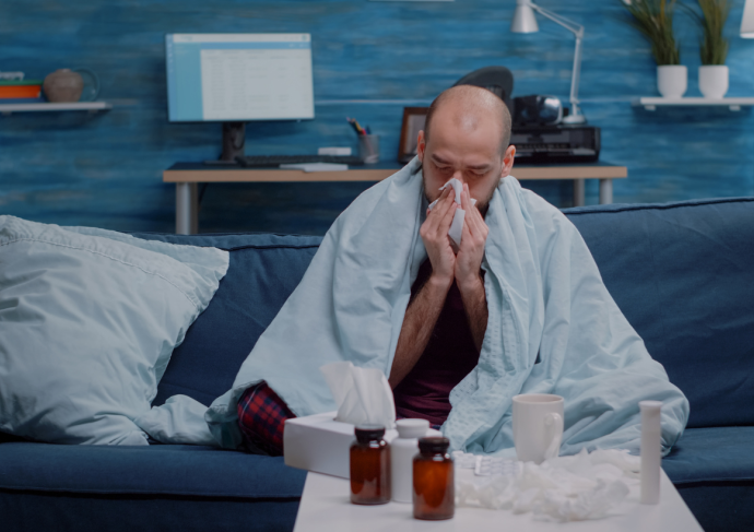 Man sitting on the couch at night blowing his nose