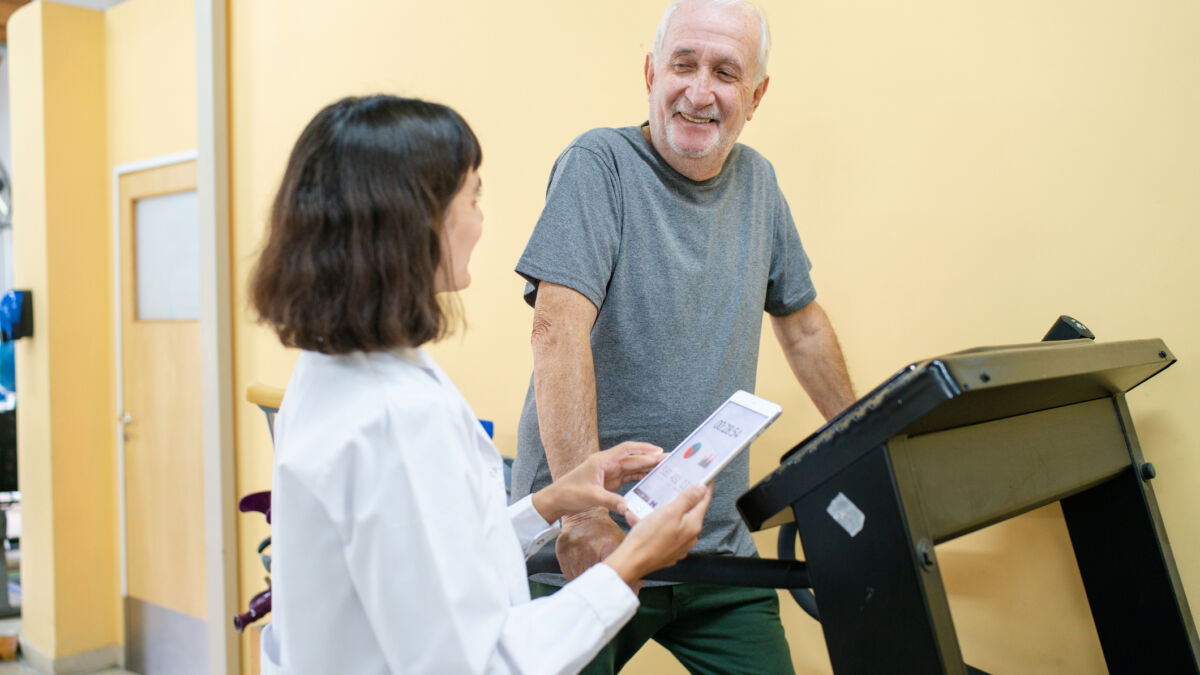 Man walking on treadmill at hospital talking with his female doctor.