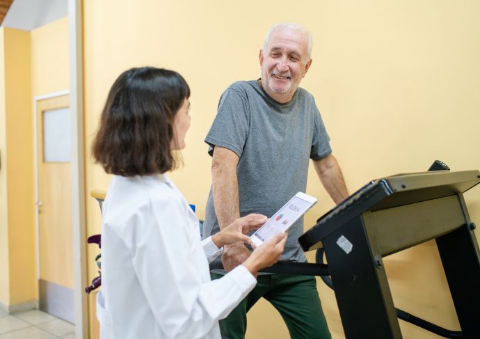 Man walking on treadmill at hospital talking with his female doctor.