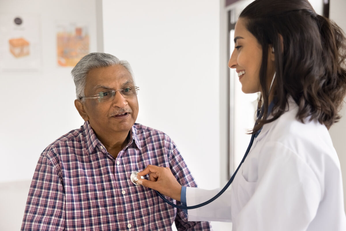 Female cardiologist holding stethoscope on older mans chest