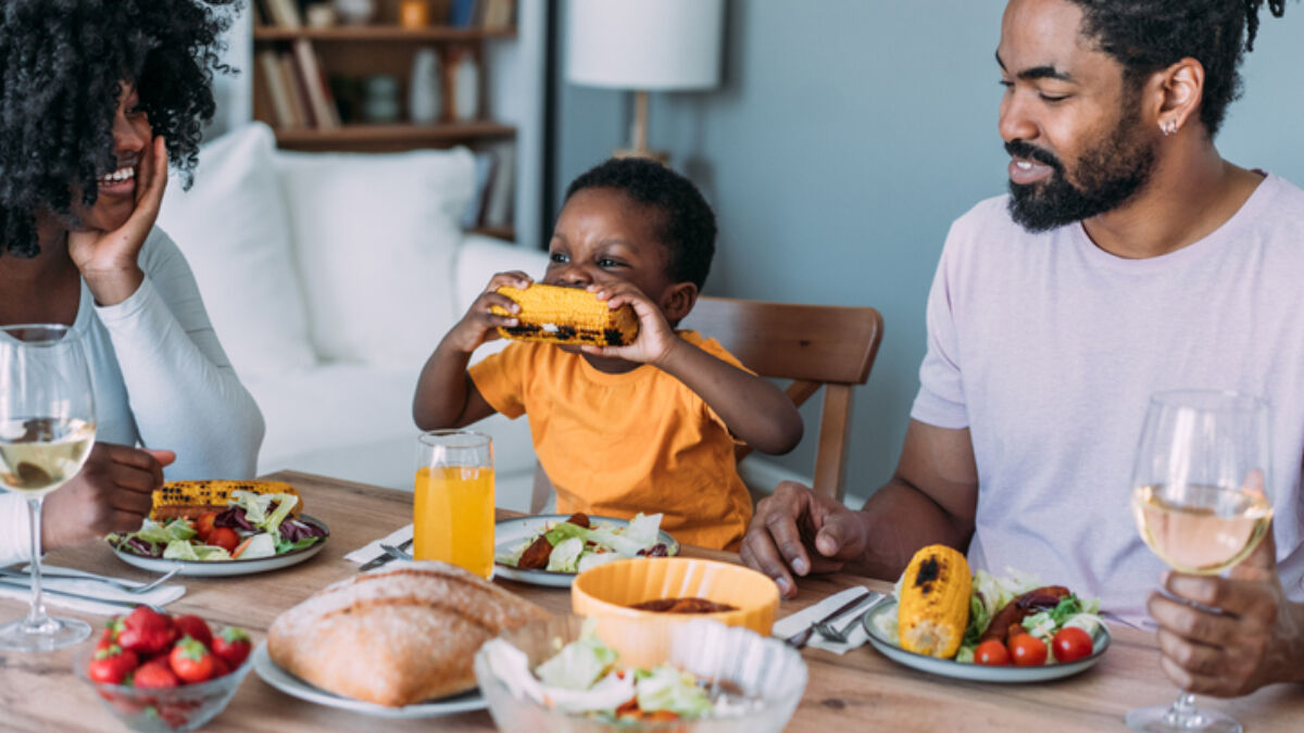 Family eating dinner and smiling at boy eating corn