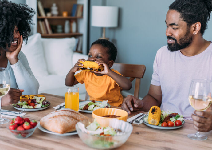 Family eating dinner and smiling at boy eating corn