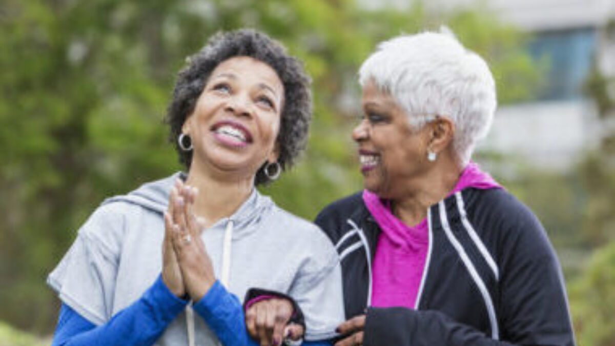 Two older women talking and walking outside holding hands.