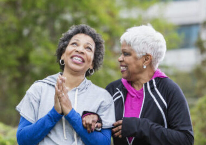 Two older women talking and walking outside holding hands.