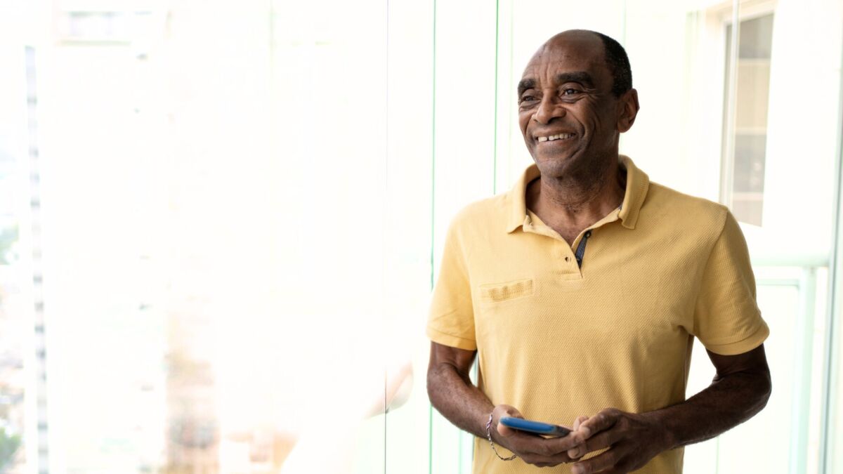 Smiling man next to window with phone in hand