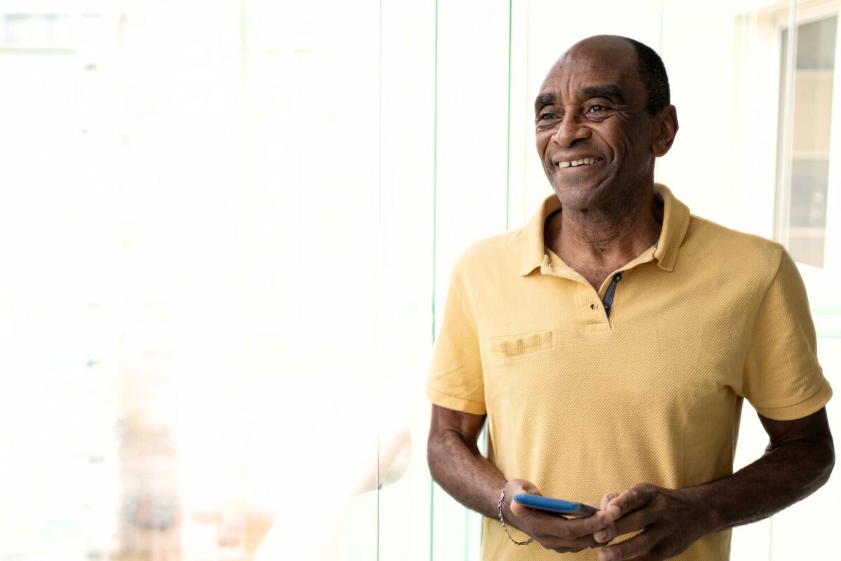 Smiling man next to window with phone in hand