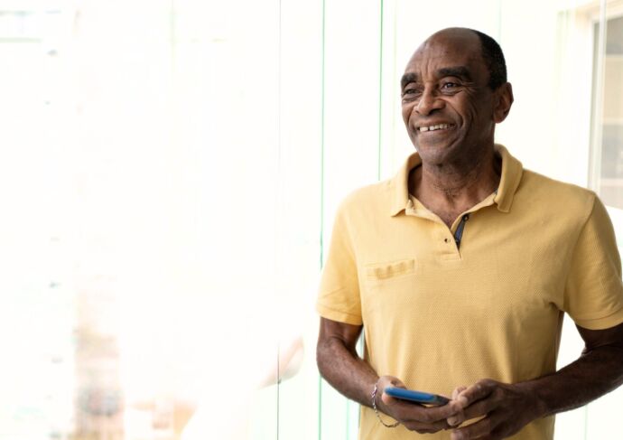 Smiling man next to window with phone in hand