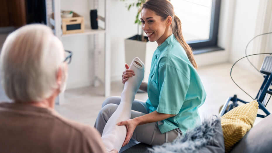 Smiling nurse assisting elderly male with compression stockings