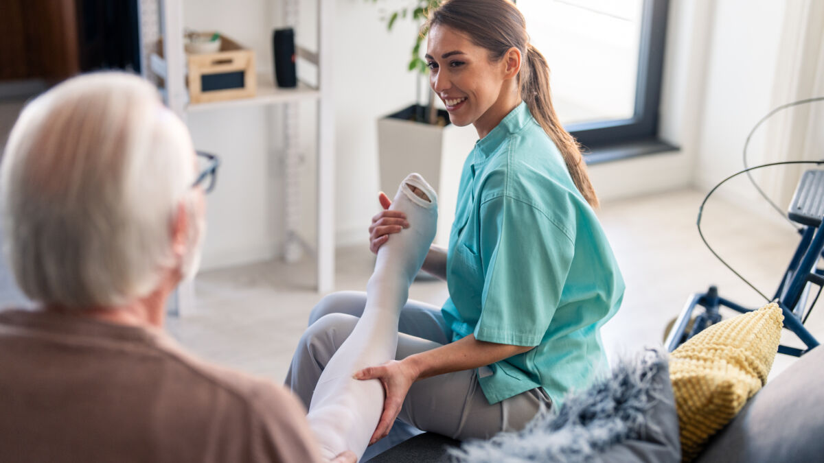 Smiling nurse assisting elderly male with compression stockings
