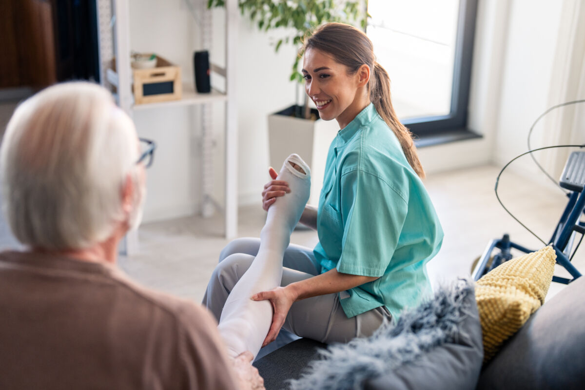 Smiling nurse assisting elderly male with compression stockings