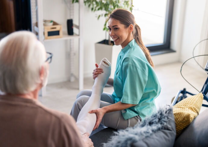 Smiling nurse assisting elderly male with compression stockings