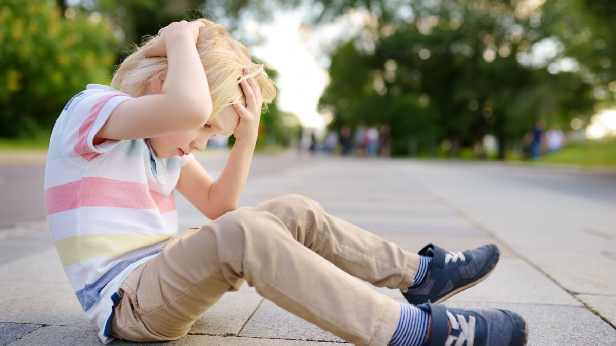 Boy sitting on the street holding his head