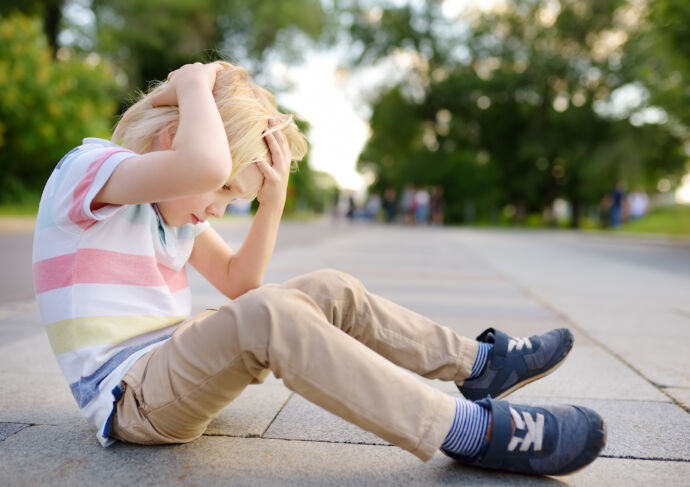 Boy sitting on the street holding his head