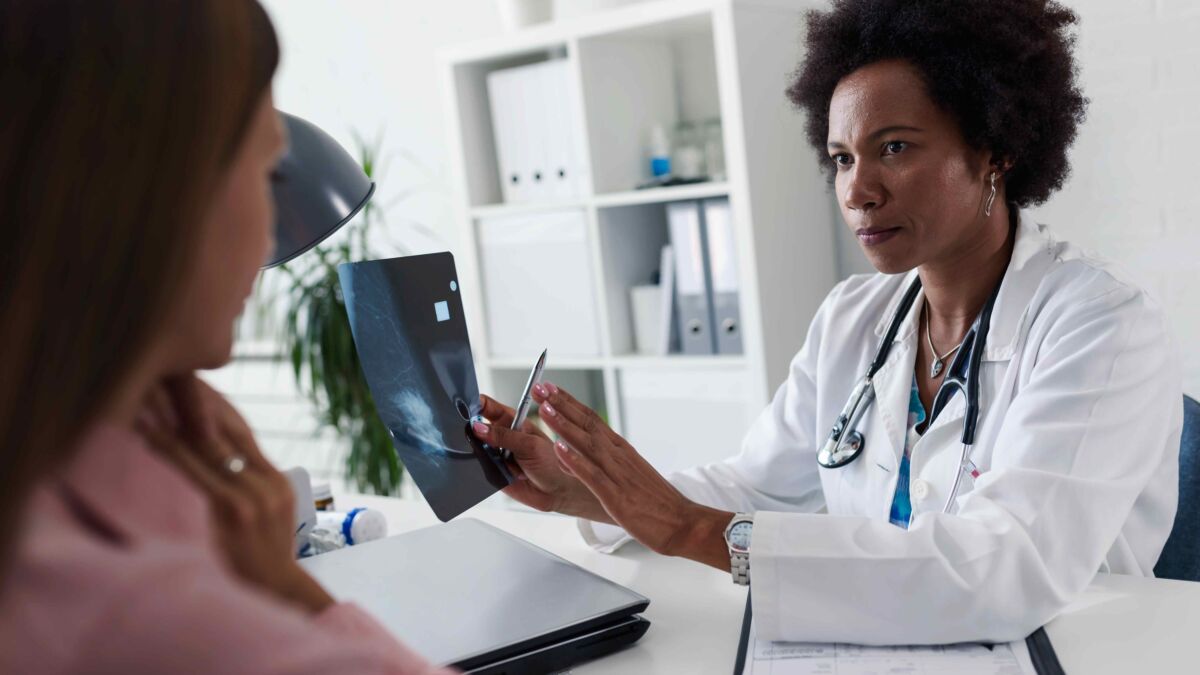 Female doctor sitting at desk talking to female patient while looking at her mamogram