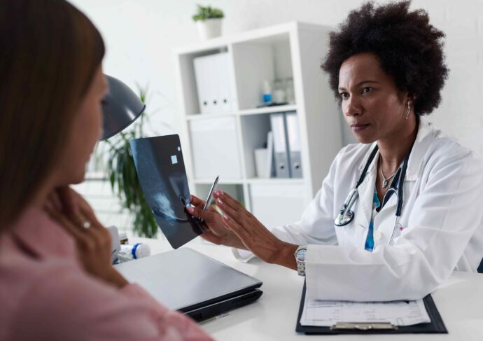 Female doctor sitting at desk talking to female patient while looking at her mamogram