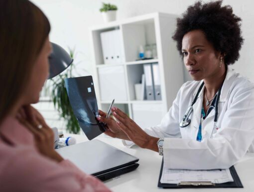 Female doctor sitting at desk talking to female patient while looking at her mamogram