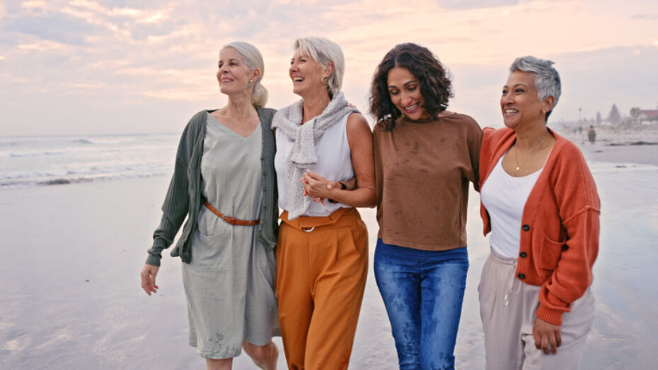 Four middle aged women smiling while walking on beach