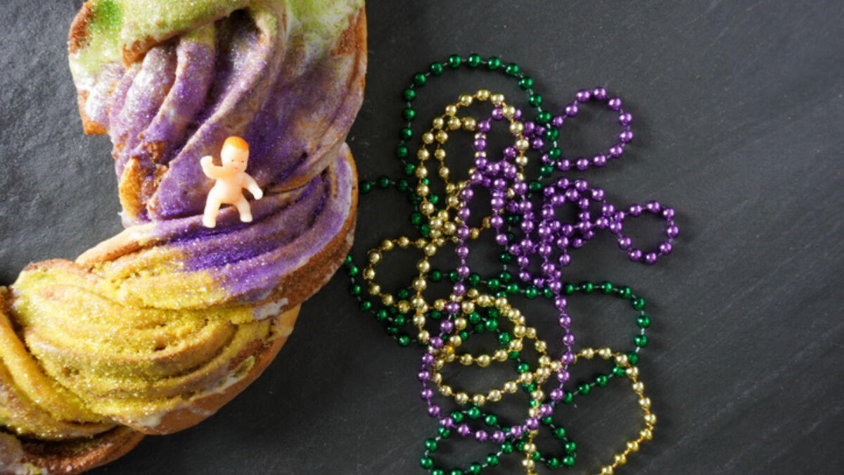 King cake with baby on top and purple green and gold beads