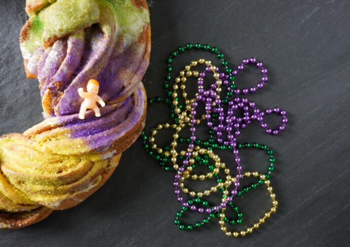 King cake with baby on top and purple green and gold beads
