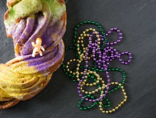 King cake with baby on top and purple green and gold beads