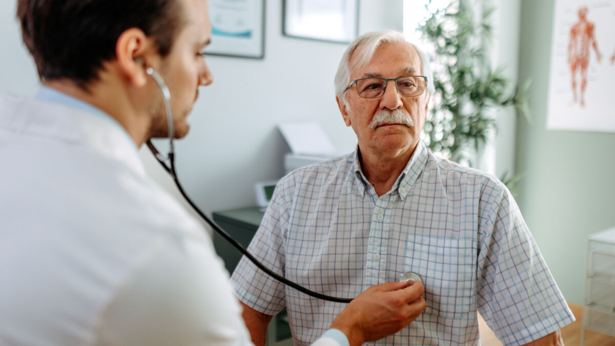 Older man in doctors office and his doctor listening to his heart with stethoscope