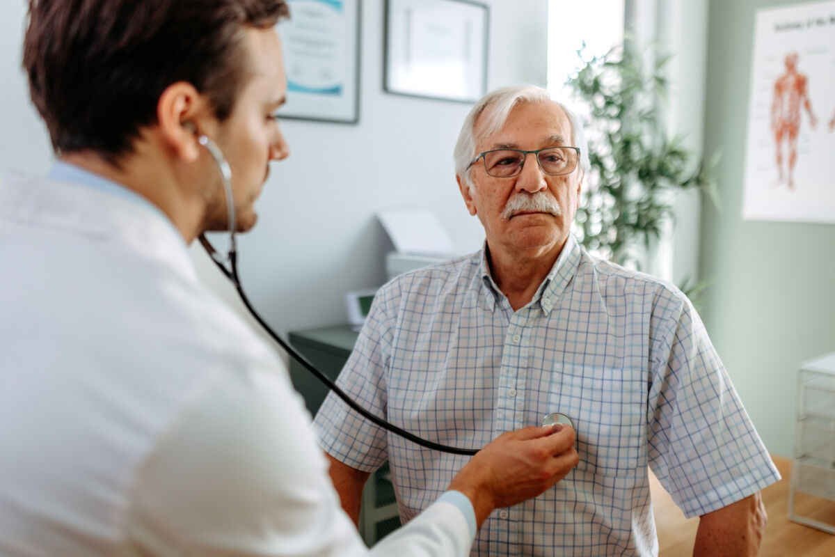 Older man in doctors office and his doctor listening to his heart with stethoscope