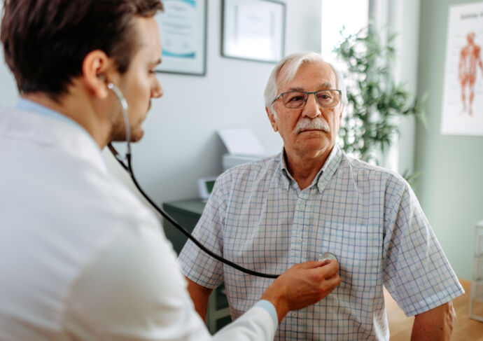 Older man in doctors office and his doctor listening to his heart with stethoscope