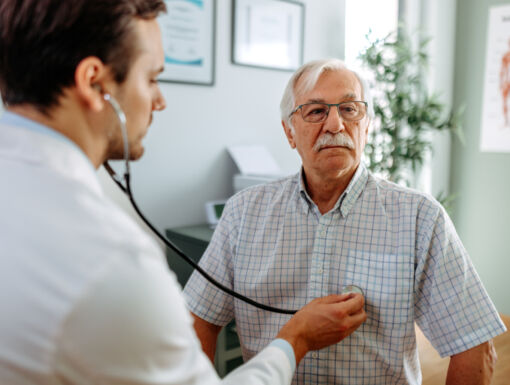 Older man in doctors office and his doctor listening to his heart with stethoscope