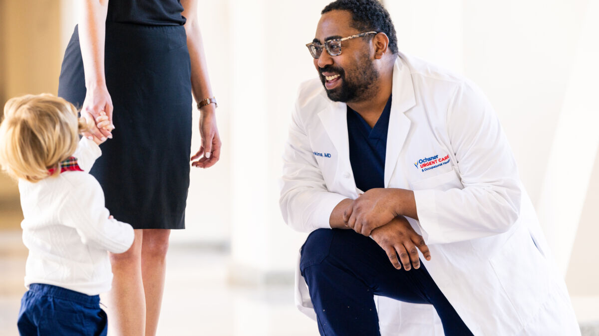 Doctor smiling and kneeling to talk to child and their mom