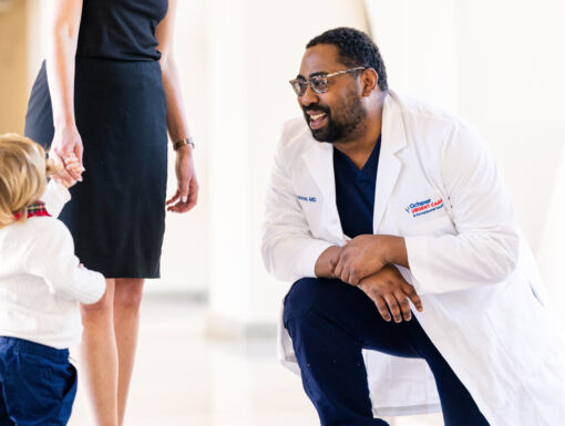 Doctor smiling and kneeling to talk to child and their mom
